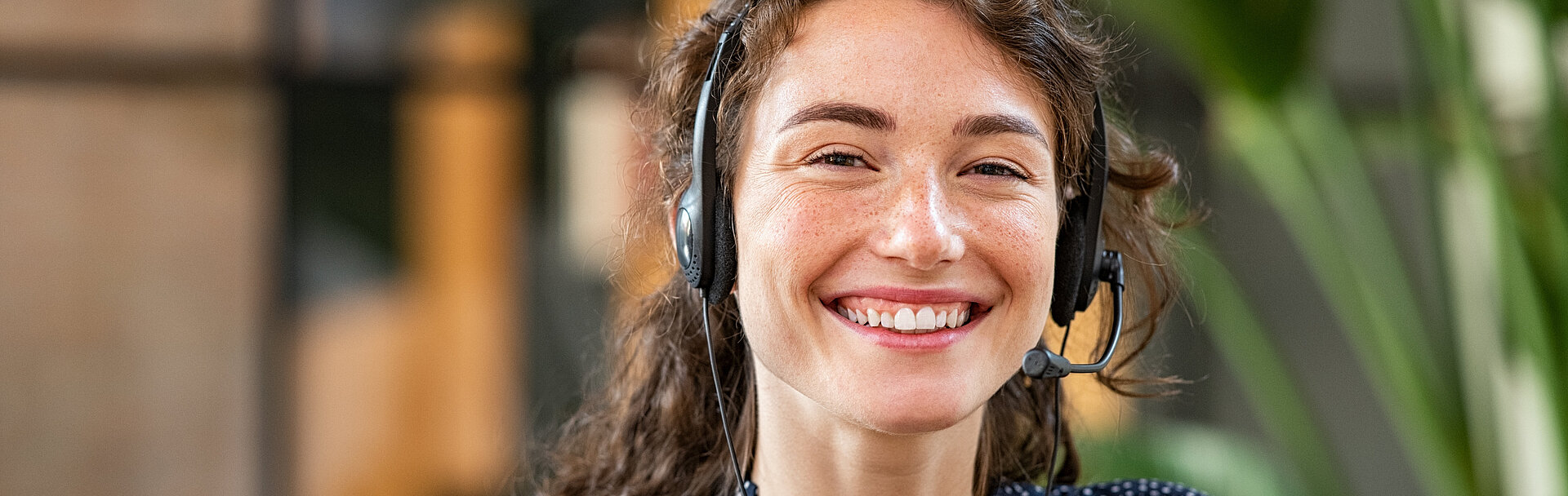 Portrait einer lächelnden jungen Frau, welche Businesskleidung und ein Headset trägt.